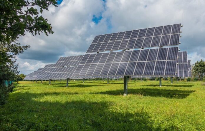 photovoltaic-system-2742302_1920 Un campo con múltiples paneles solares montados sobre soportes metálicos, frente a un cielo parcialmente nublado. Los árboles son visibles al fondo.