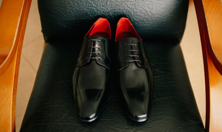 Un par de zapatos de vestir de cuero negro con interiores rojos se colocan sobre una silla de cuero negro.